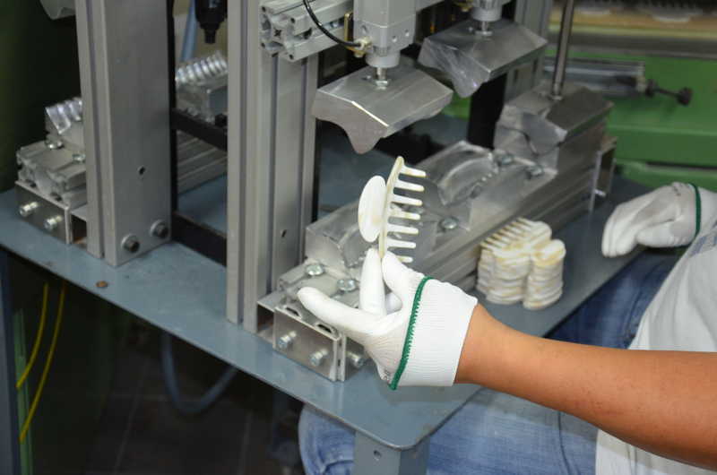 Artisan holding a shaped cellulose acetate hair claw in front of the forming press